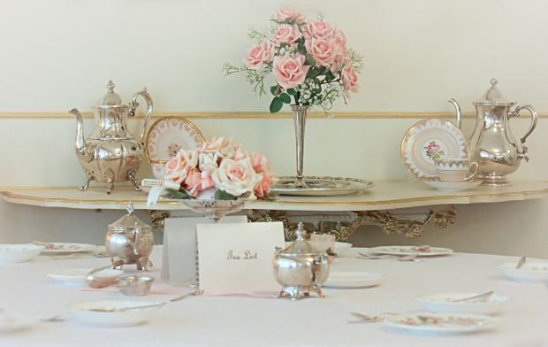 Silver floral table centerpiece with pink roses, elegant vintage tea set, and fine china for wedding or event decor in Winnipeg.