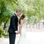 Elegant newlywed couple sharing a kiss outdoors at a wedding venue in Winnipeg, showcasing romantic wedding moments.