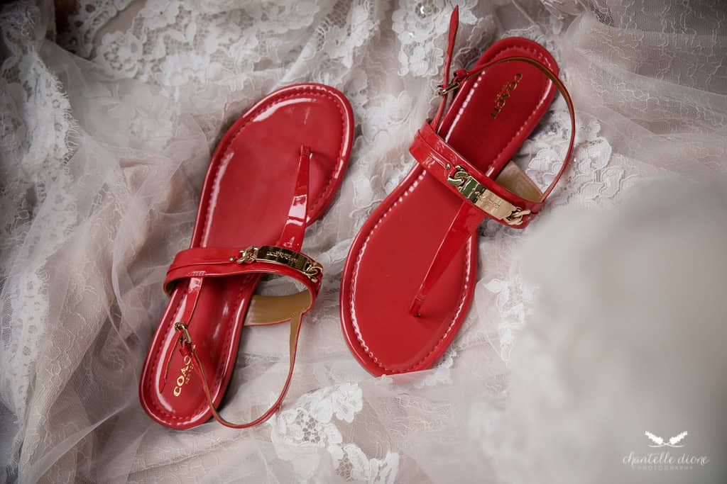 Red patent leather sandals with gold accents on delicate lace fabric.