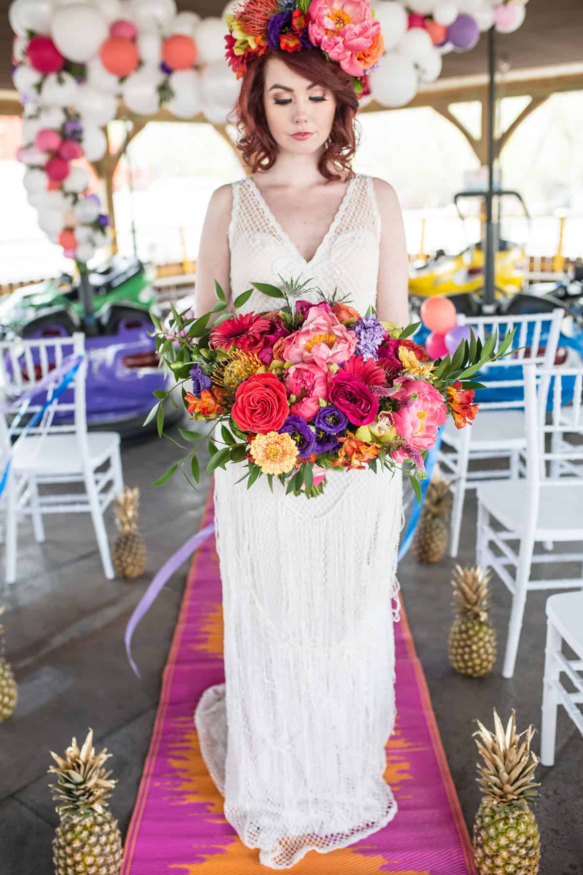 Vibrant bridal bouquet with pink, purple, orange, and yellow flowers at a colorful outdoor wedding decorated with pineapples and balloons.