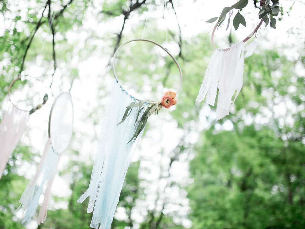 Dreamcatchers hanging on trees with lace and floral accents, perfect for organic outdoor wedding decor in Winnipeg.