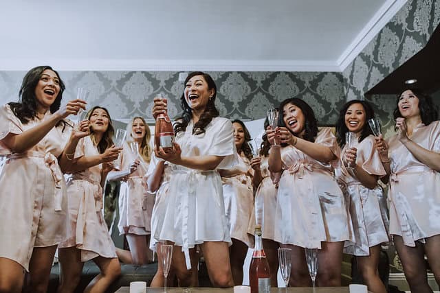 Happy bridesmaids celebrating with champagne before wedding in a stylish indoor setting.