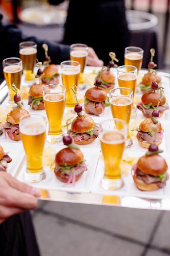 Artisanal sliders with mini glasses of beer on serving tray at wedding reception.