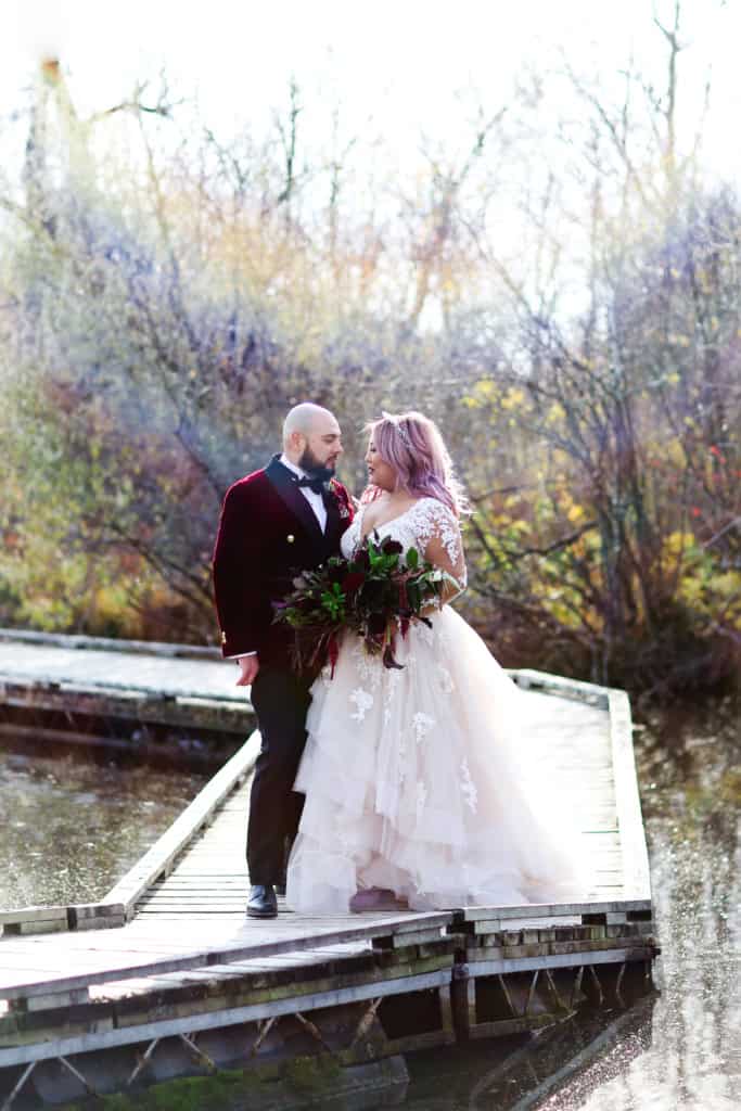 Elegant wedding couple standing on a wooden dock by the water in outdoor autumn setting, perfect for Winnipeg wedding and event photography.