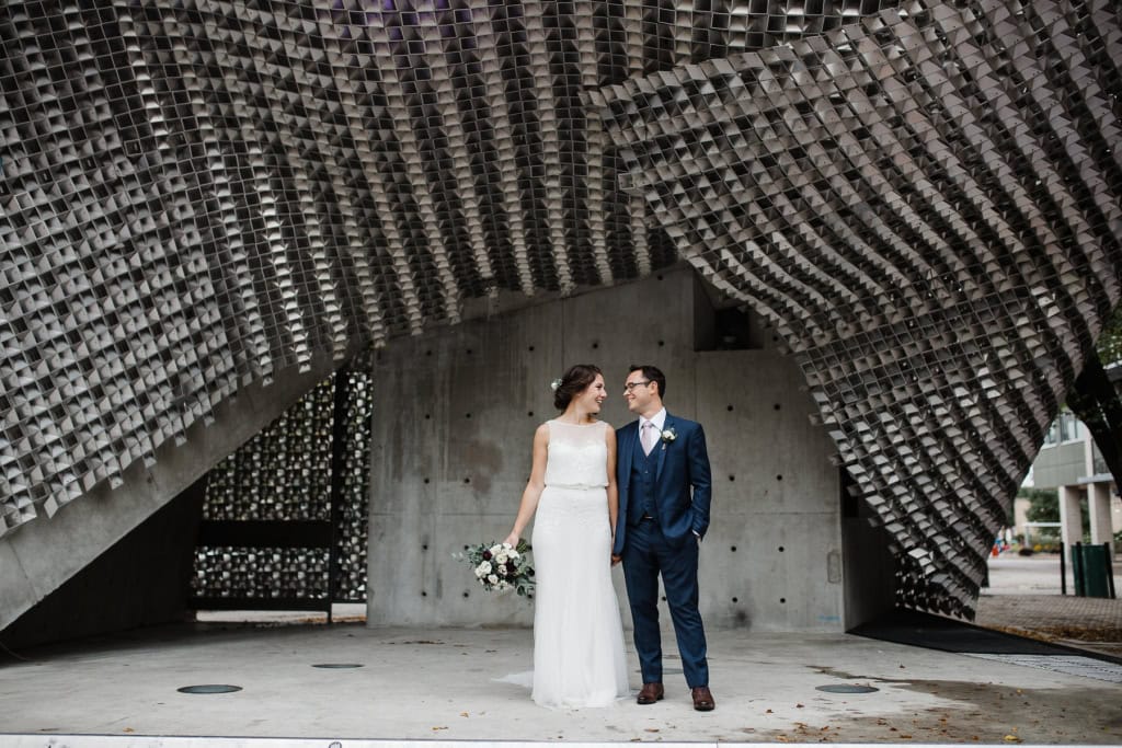 Elegant wedding couple standing under contemporary architectural structure in Winnipeg.
