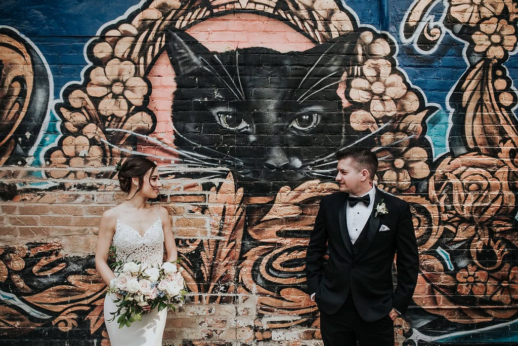 Black cat mural with floral accents on brick wall, featuring a bride and groom in wedding attire.