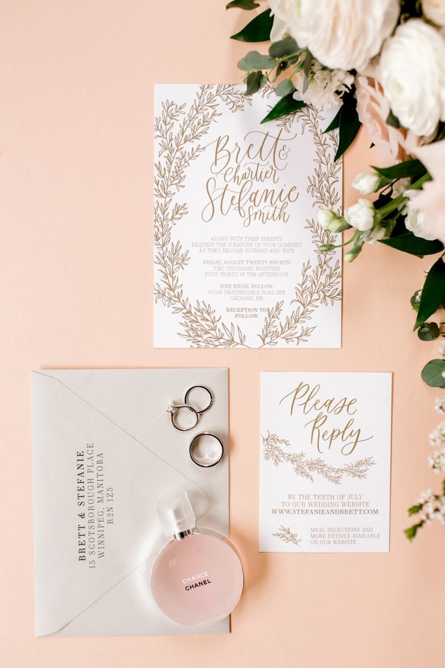 Elegant wedding invitation suite with floral design, featuring a Save the Date card, RSVP card, and wedding details, complemented by wedding rings and perfume on a soft pink background.