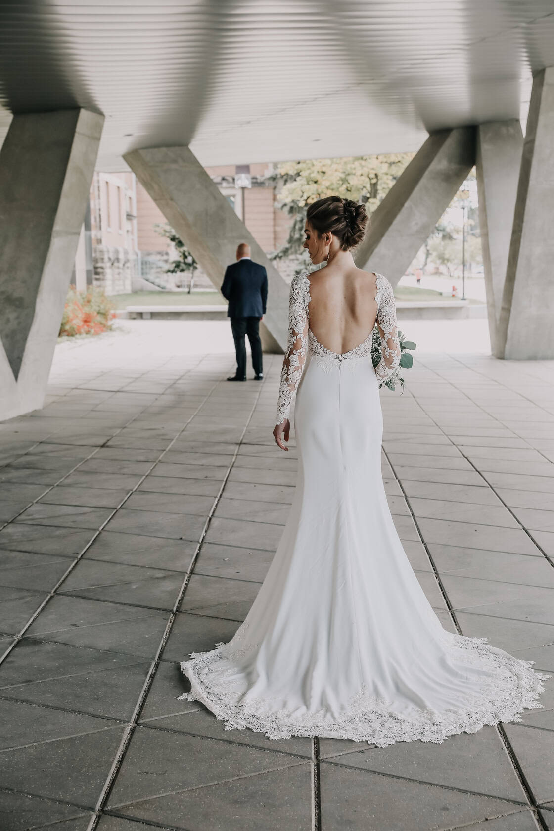 Elegant bride in a lace back wedding gown under modern architectural structure at Winnipeg wedding venue.