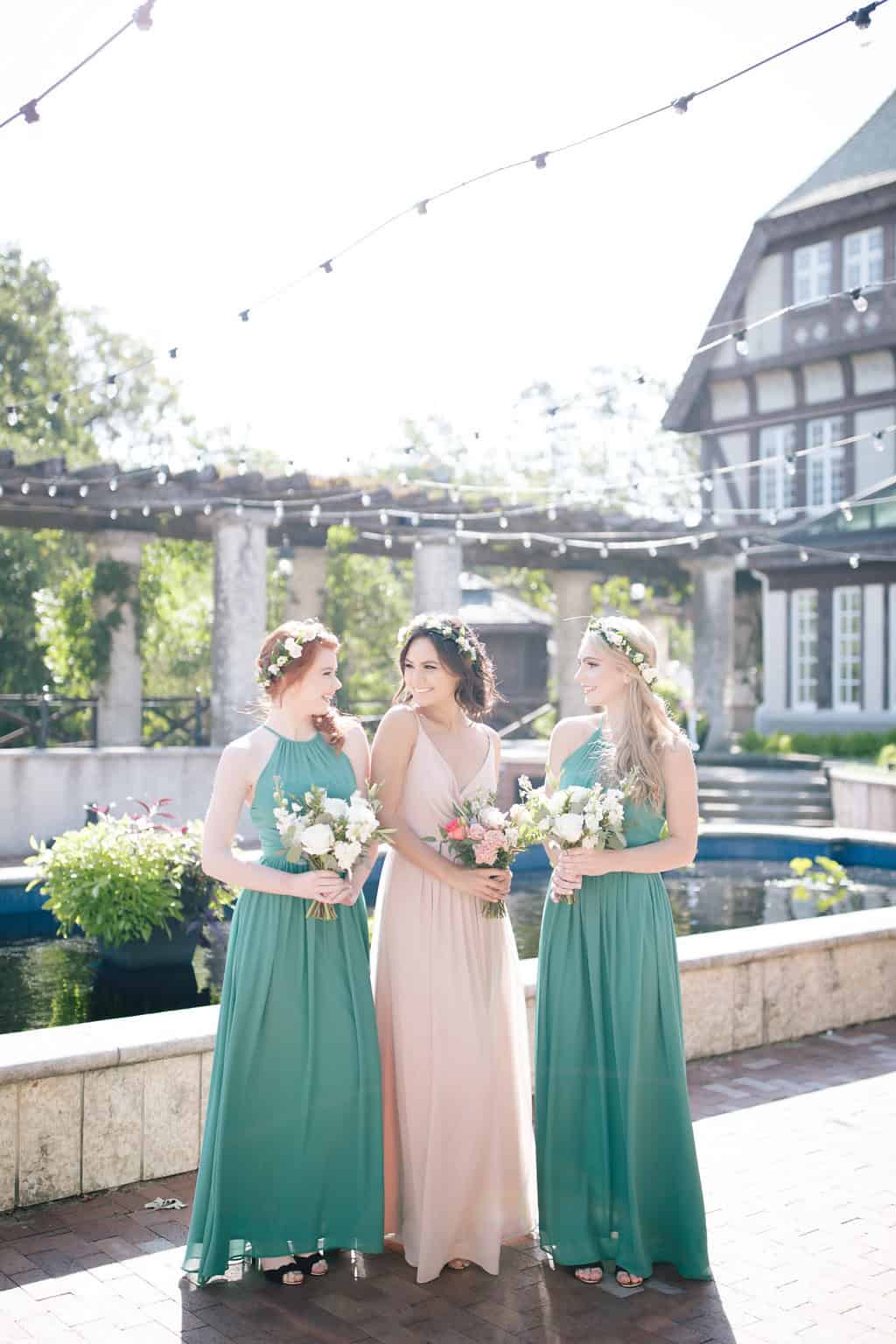Elegant wedding bridesmaids and bride smiling outdoors with floral crowns and bouquets during a sunny day at a beautifully decorated event venue in Winnipeg.
