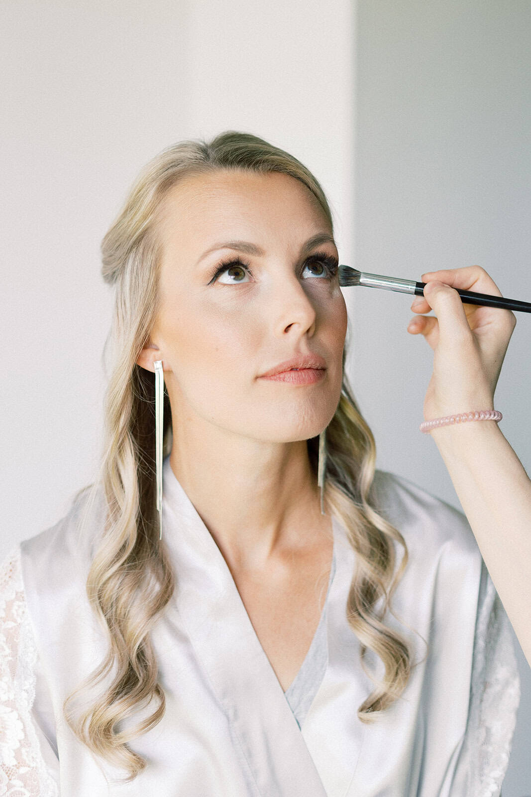 Bridal makeup artist applying makeup to a bride in a bright room at Melanie Parent Events, Winnipeg wedding and event planning services.