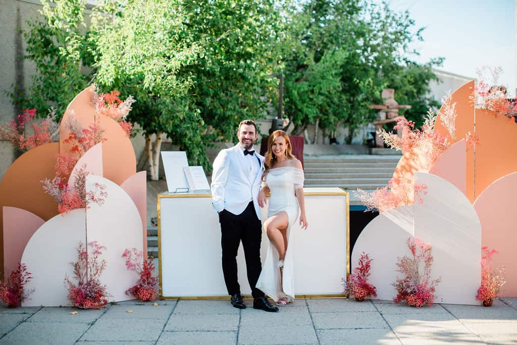 Elegant wedding couple at outdoor reception with floral decor, greenery, and modern backdrop in Winnipeg. Perfect wedding setup captured in natural sunlight.