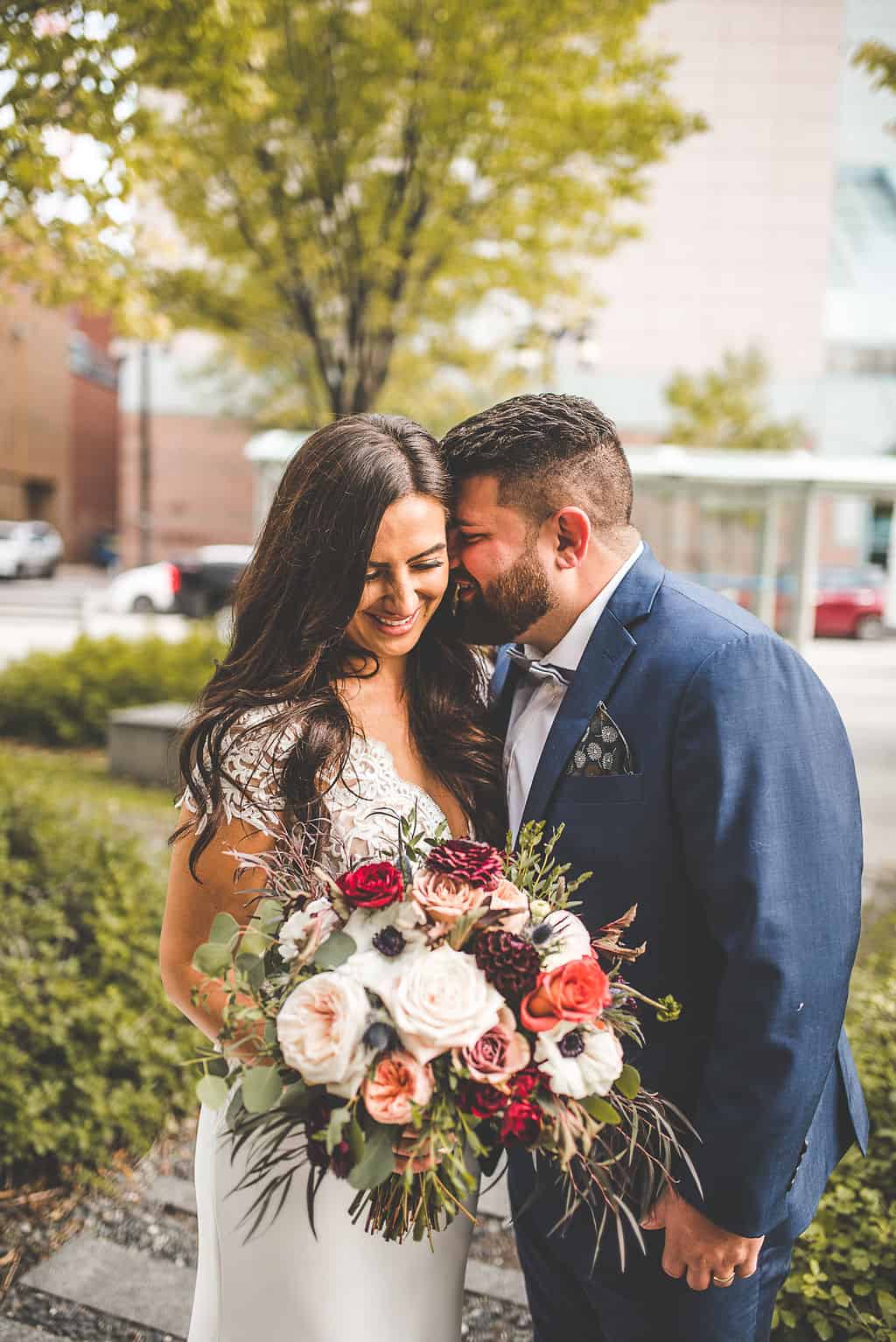 A couple sharing an intimate moment outdoors with a beautiful bouquet, celebrating their wedding day in Winnipeg, featuring wedding planning by Melanie Parent Events.