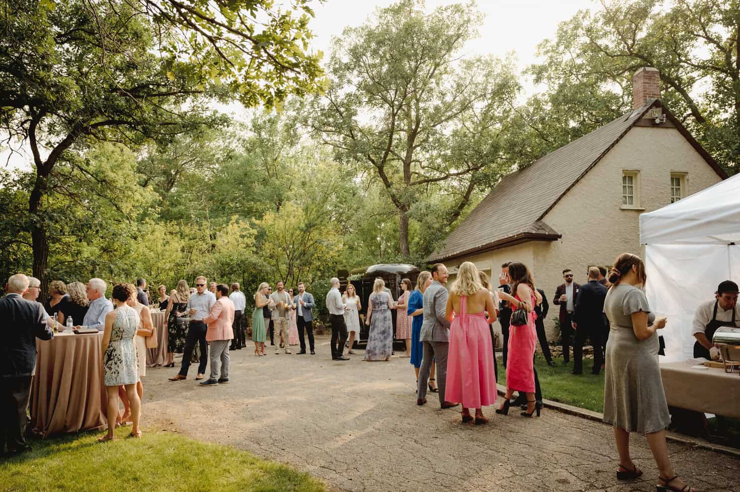 Elegant outdoor wedding reception with guests socializing under large leafy trees at Melanie Parent Events in Winnipeg.