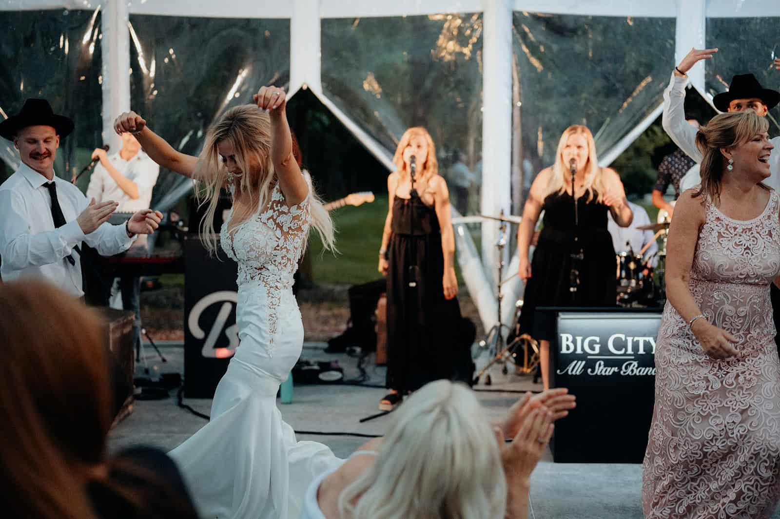 Elegant bride dancing at outdoor wedding reception with live band, guests celebrating, and joyful atmosphere at Melanie Parent Events in Winnipeg.