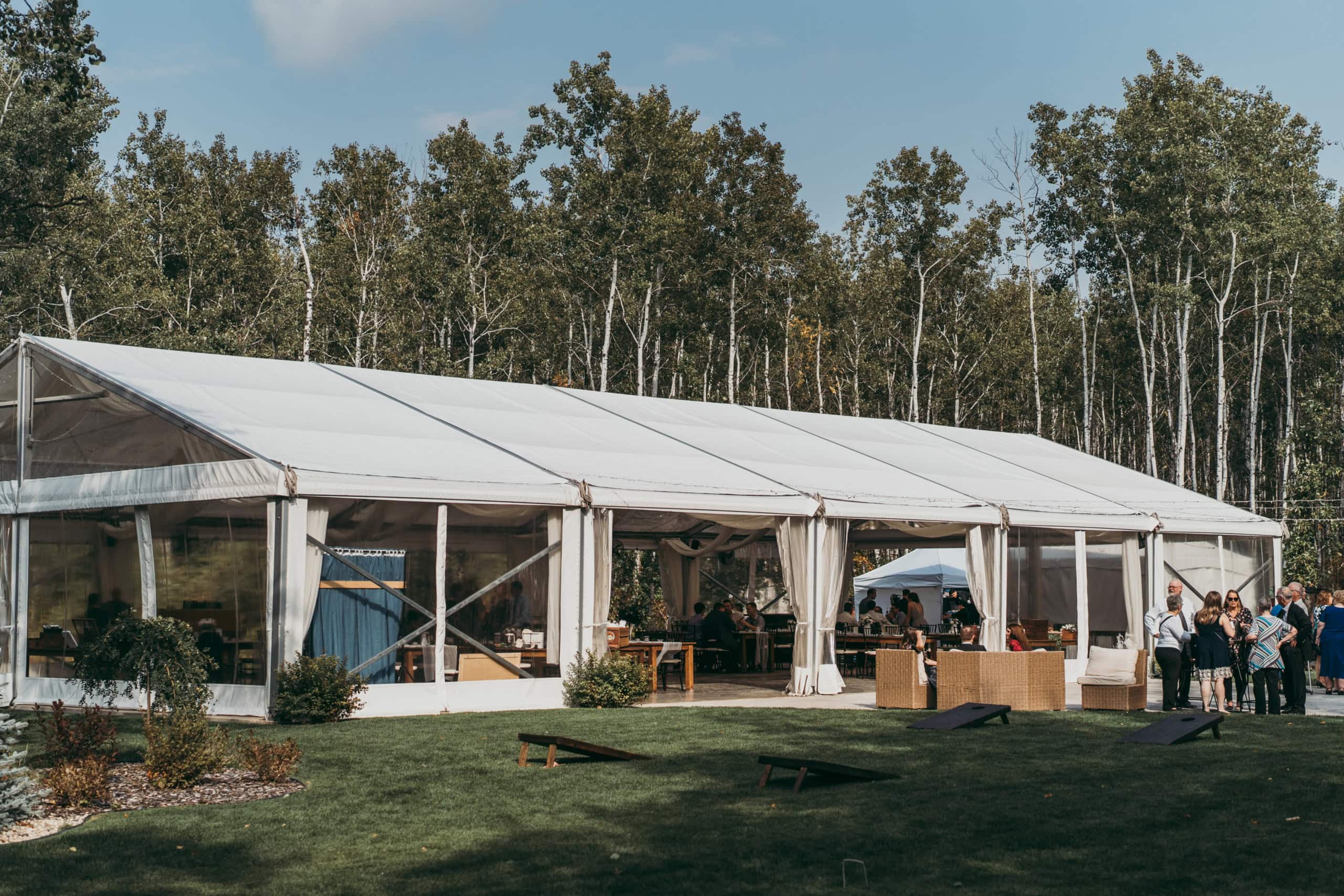 Elegant outdoor wedding reception setup in a large white tent surrounded by lush trees in Winnipeg. Perfect for hosting memorable events with beautiful natural scenery.