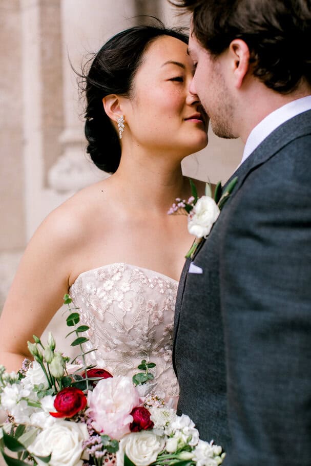 Elegant wedding couple sharing a close moment during their ceremony, with the bride holding a beautiful floral bouquet and the groom dressed in a dark suit.