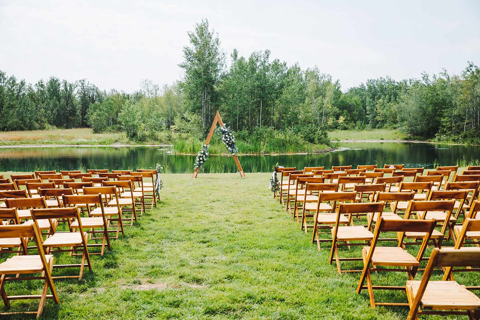 Breathtaking outdoor wedding ceremony setup by a tranquil lake surrounded by lush greenery in Winnipeg. Perfect for romantic and all-natural weddings.