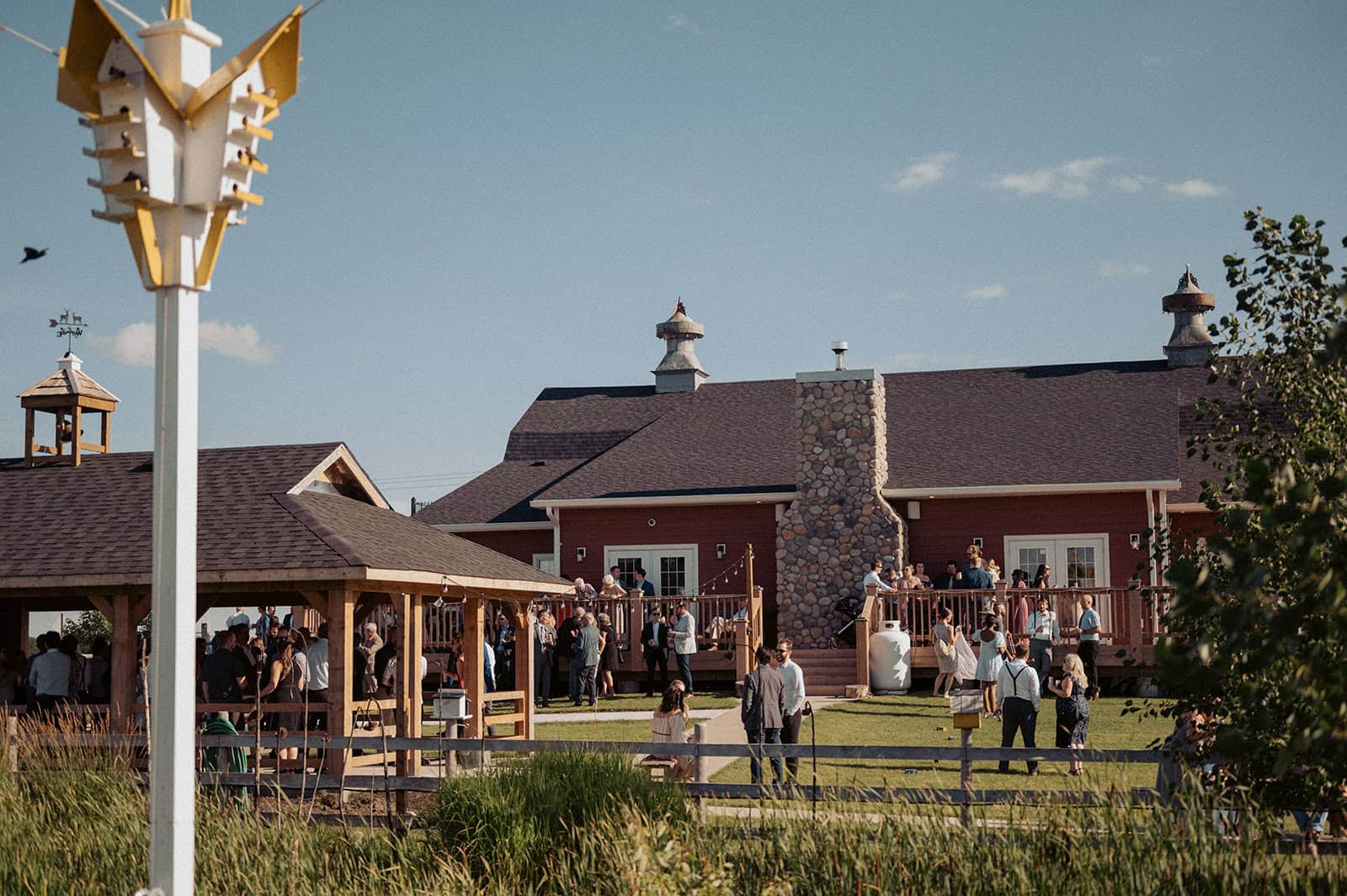 Outdoor wedding reception at Melanie Parent Events in Winnipeg, featuring a rustic barn, outdoor seating, and guests enjoying a celebration under a bright blue sky.