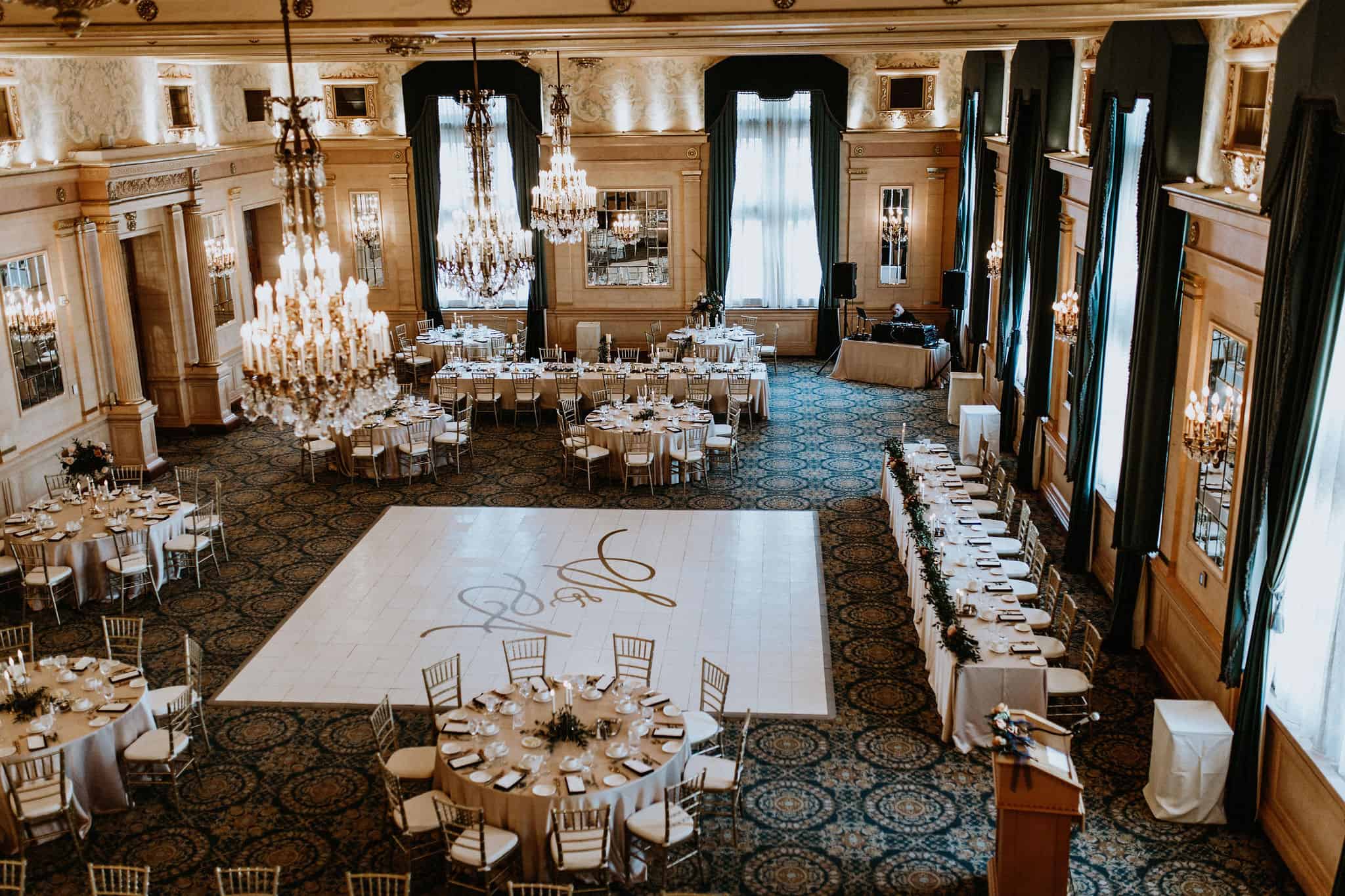 Elegant wedding reception hall with chandeliers, beautifully set round tables, and a dance floor for a Winnipeg wedding event.