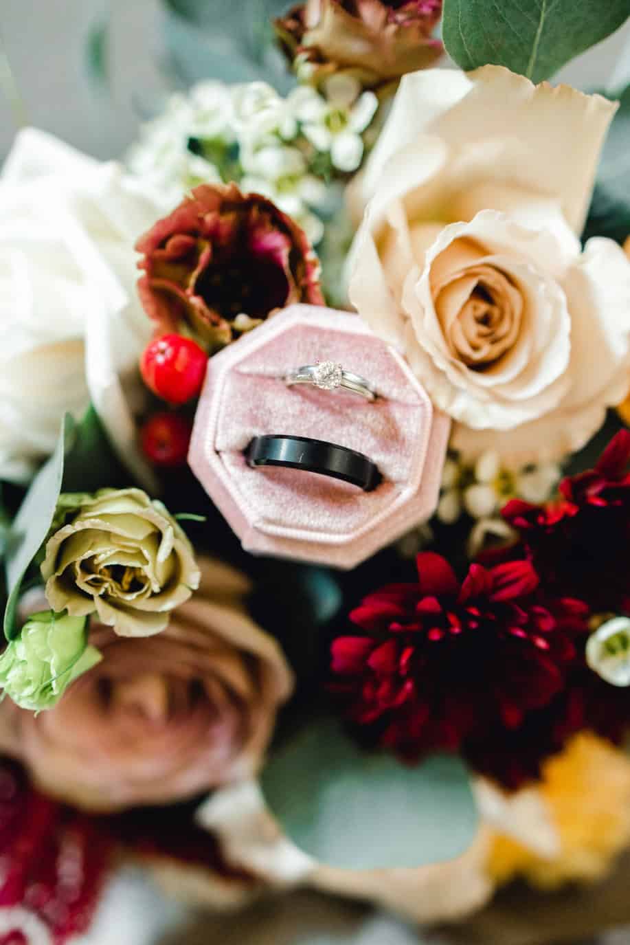 Luxurious wedding rings displayed on a pink velvet ring box surrounded by vibrant flowers.