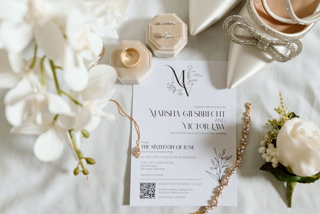 Elegant wedding invitation with floral design, jewelry, and ceremony details on a white table setting.