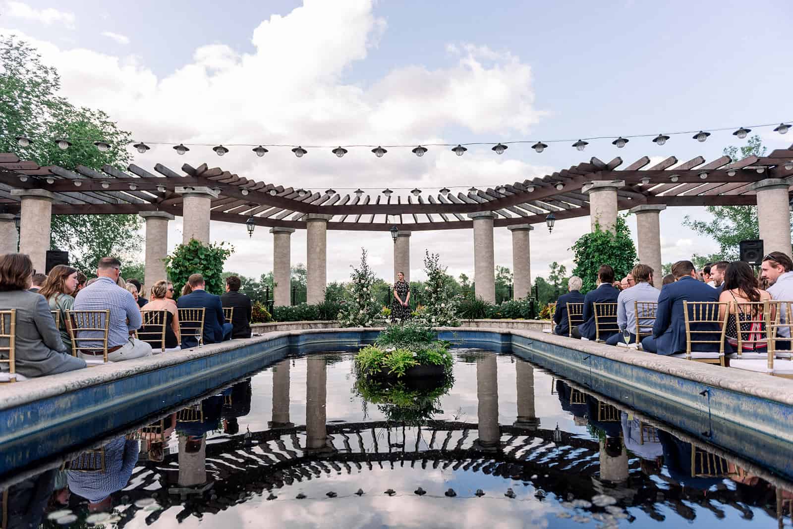 Elegant outdoor wedding ceremony at a scenic venue with a reflecting pool and chandelier string lights in Winnipeg.
