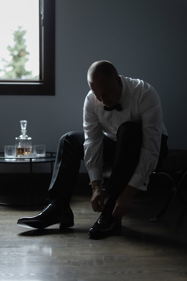 Elegant man in formal attire tying his shoelaces in a dimly lit room.