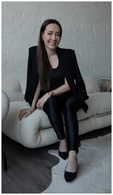 Elegant woman in black business attire sitting on a modern white sofa in a stylish indoor setting.